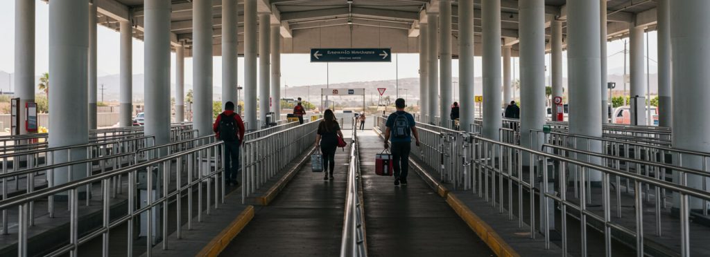 Daytime pedestrian border crossing to Mexico with travelers and cooler bags, illustrating how medical tourism and insurance planning supports safe, documented same-day pharmacy trips.
