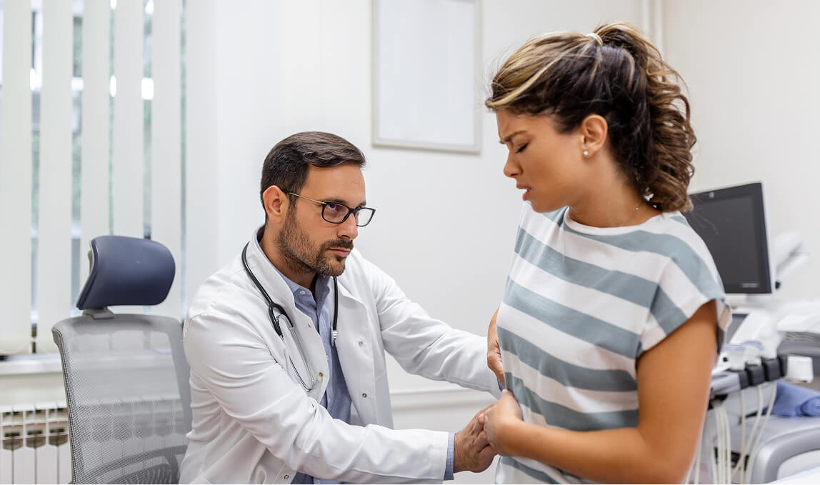 Specialist doctor examining a female patient's abdomen for liver-related symptoms associated with Hepatitis C during a clinical consultation