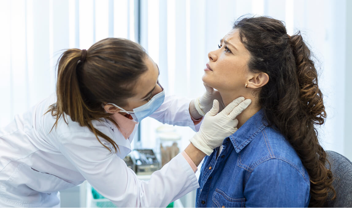 Doctor with gloves and mask carefully examining a female patient's neck and thyroid area for signs of thyroid cancer